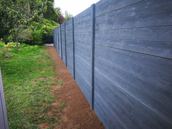 Clôture sur mesure en bois gris anthracite sans jointures, bordant un chemin de jardin dans un espace verdoyant.